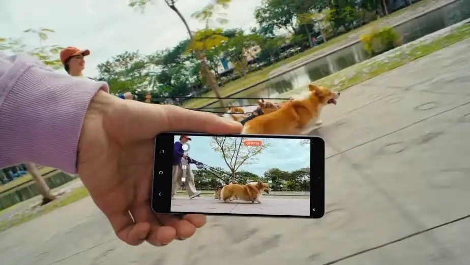 Kézben tartott Galaxy S26 Ultra telefonnal videóznak egy futó corgit a parkban.